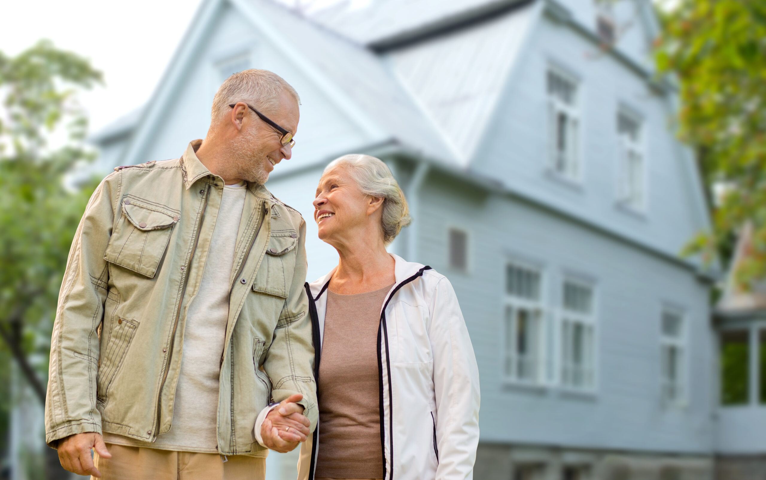 happy senior couple holding hands over house